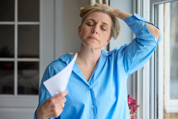 ménopause femme mature ayant des bouffées de chaleur à la maison se rafraîchissant avec des lettres ou des documents - menopause photos et images de collection