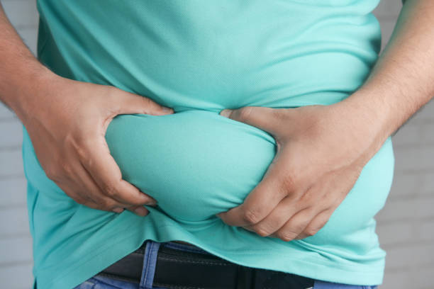 main de l’homme tenant une graisse abdominale excessive, concept de surpoids - obesity photos et images de collection
